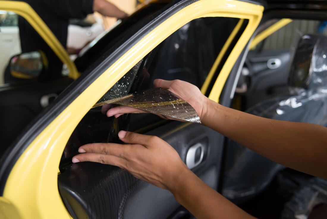 Picture of a yellow car door with a person applying tint to the window