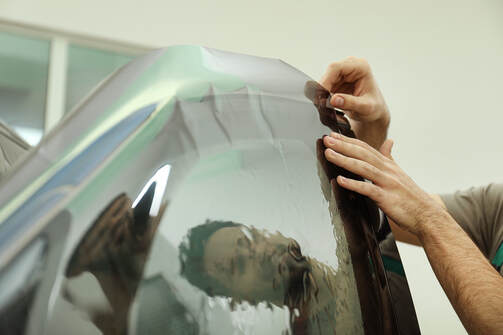 Picture of a guy putting heat resistant film on the window of a car