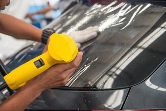 Picture of a yellow heat gun applying tint to a car's rear windshield